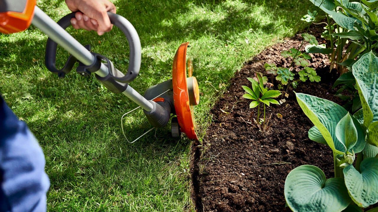 Automower working on downhill in a backyard with a house in the background